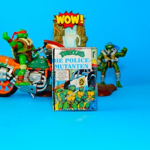 Può includere: Un'immagine vivace con action figure dei Teenage Mutant Ninja Turtles e un fumetto. Le figure sono verdi, una su una moto. La copertina del fumetto recita "Turtles Die Police-Mutanten" con un'illustrazione di un'auto della polizia. Un cartello "WOW!" è sullo sfondo.