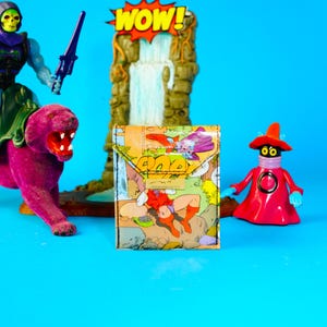 Könnte beinhalten: Eine farbenfrohe Geldbörse mit Comic-Illustration und Klappenverschluss. Das Bild zeigt Actionfiguren von Zeichentrickfiguren, darunter ein lila Panther, eine rote Figur und ein grüner und lila Bösewicht.