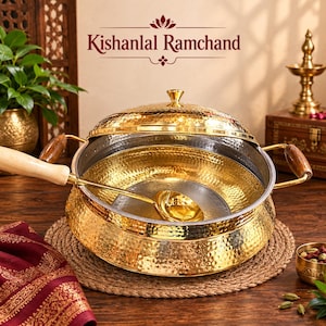 Puede incluir: Una olla de servicio de latón martillado con tapa a juego y dos asas laterales, acompañada de un cucharón de latón con mango de madera clara. La olla presenta el texto Kishanlal Ramchand. El exterior es de latón pulido y el interior es plateado.
