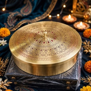Könnte beinhalten: Ein runder Messingbehälter mit einem Deckel, der ein kompliziertes graviertes Mandalamuster und einen kleinen zentralen Knopf aufweist. Der Text "Kishan Lal Ramchandra" steht in einer dekorativen Schriftart über dem Metallbehälter.