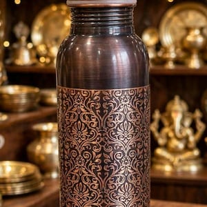 May include: A cylindrical copper water bottle featuring a dark, brushed finish and an intricate, repeating floral pattern etched into the lower body. The bottle has a smooth, rounded cap and a narrow neck, showcasing a metallic, reddish-brown hue.