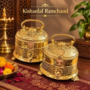 Puede incluir: Dos recipientes de metal dorado con asas y patrones en relieve intrincados. Cada recipiente cuenta con una tapa con bisagras y un mecanismo de cierre. El texto "Kishanlal Ramchand" aparece en letras doradas sobre los recipientes.