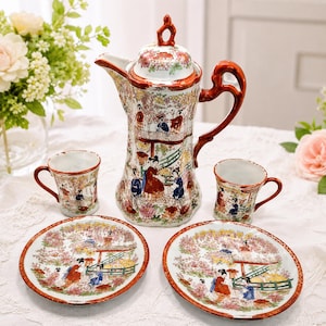 May include: A porcelain tea set featuring a tall teapot with a lid, two small cups, and two saucers. Each piece is decorated with a colorful scene of figures in a garden with cherry blossoms, accented by a deep orange-red trim on the edges and handles.