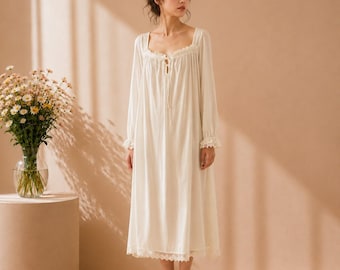 May include: A long-sleeved, ankle-length cream nightgown featuring a square neckline with delicate lace trim, a gathered bodice, and a tie closure at the center chest. The garment has cuffed sleeves with lace detailing and a scalloped lace hem.