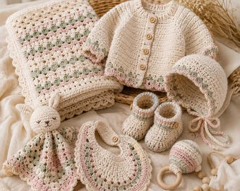 Peut inclure: Un ensemble de bébé au crochet comprenant une couverture crème, un gilet à manches longues avec des boutons en bois, un bonnet à nouer, des chaussons, un bavoir, un doudou lapin et un hochet avec anneau en bois, rehaussés de rose et vert sauge.