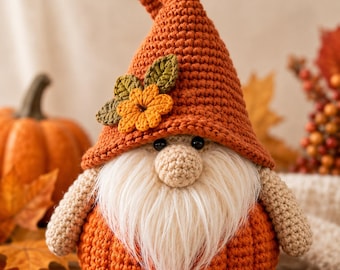 Peut inclure: Une figurine de gnome au crochet avec un grand chapeau pointu orange orné d'une petite fleur orange et de deux feuilles vertes. Le gnome possède un nez beige rond, une longue barbe en fausse fourrure blanche et un corps en forme de citrouille.