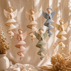 May include: Six hanging crochet angel ornaments in various pastel colors including cream, light pink, sage green, and dusty blue. Each angel features a wooden bead head, a halo, wings, and a spiraling dress, all suspended by thin white strings.