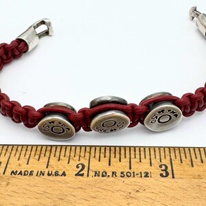 May include: A red leather bracelet with silver metal charms. The charms have the word "OSCAR" engraved on them.