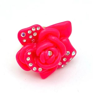 May include: A pink rose-shaped ring with clear rhinestones.