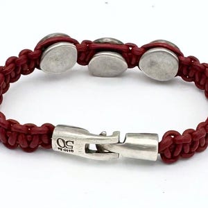 May include: A red leather bracelet with silver metal accents and a clasp that reads "U.S. ORIGIN".