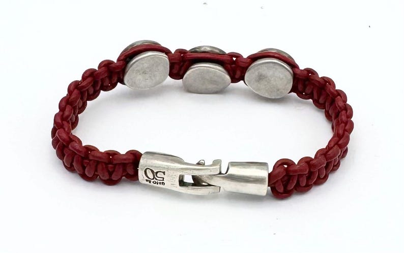 May include: A red leather bracelet with silver metal accents and a clasp that reads "U.S. ORIGIN".