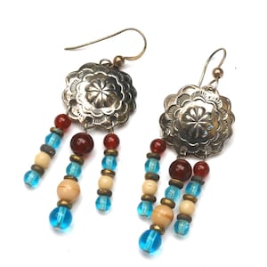 May include: Silver dangle earrings with blue, white, and red beads. The earrings feature a silver disc with a floral design.