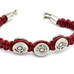 May include: Red leather bracelet with three silver round charms that say "OMA" on them.