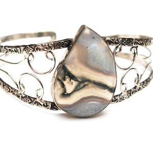 May include: A silver bracelet with a delicate filigree design and a large, teardrop-shaped agate stone in the center. The stone has a white, gray, and black pattern.