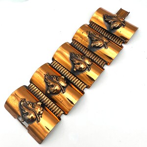 May include: A copper-toned bracelet with a series of curved rectangular links. Each link features a raised oak leaf design. The bracelet has a clasp closure. The overall design is vintage and decorative.