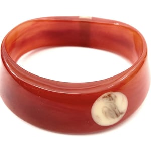May include: A red plastic bangle bracelet with a white circular design in the center.