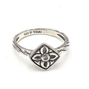 May include: A silver ring with a square-shaped design featuring a flower with a small, clear stone in the center. The ring is marked "925 THAI" on the inside.