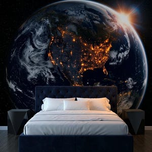 May include: A bedroom featuring a dark blue upholstered bed with white bedding, flanked by two black geometric side tables. The wall behind the bed displays a large mural of Earth from space, showing the glowing lights of North America at night.