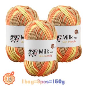 May include: Three skeins of variegated yarn in shades of tan, orange, and yellow. Each skein has a white paper label featuring a black and white cow illustration and the text Milk cot Skin-friendly. A graphic indicates 1 bag=3pcs=150g.