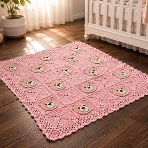 May include: A square, light pink crochet blanket featuring a repeating pattern of circular bear face appliques. Each bear face is light brown with a cream-colored muzzle, black embroidered eyes, and a black nose. The blanket has a decorative scalloped edge.