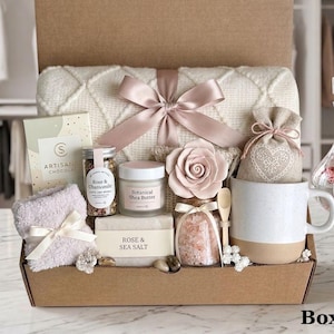 Può includere: Una scatola regalo contenente una coperta in maglia color crema con un nastro rosa, una tazza, un sacchetto con motivo a cuore, un ornamento a forma di rosa, un barattolo di sali da bagno, sapone alla rosa e sale marino, burro di karité, tè e un panno morbido.