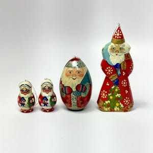 May include: Four hand-painted Christmas ornaments. Two small Matryoshka dolls, an egg-shaped Santa Claus, and a Santa Claus figure with a red coat and a green Christmas tree. Each ornament has a loop for hanging.