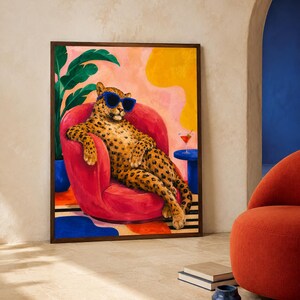 Peut inclure: Une impression d'art murale rectangulaire encadrée représentant un léopard au pelage tacheté portant des lunettes de soleil bleu vif. Le léopard est assis dans un fauteuil rouge arrondi. Une plante verte, une forme jaune et un cocktail.
