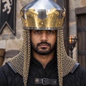 Könnte beinhalten: Ein metallischer Helm mit einer konischen Spitze aus poliertem Stahl und einem breiten, messingfarbenen Kronenband mit dekorativen Ausschnitten. Eine goldfarbene Kettenhaube hängt an der Basis des Helms, bedeckt Hals und Schultern und trägt eine schwarze Stepptunika.