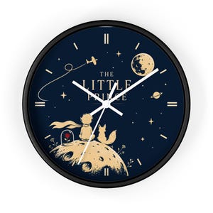 Peut inclure: Une horloge murale ronde avec un cadre noir et un cadran bleu foncé illustré en doré du Petit Prince, d'un renard, d'une rose sous cloche, d'une planète, de la lune, d'étoiles et d'un avion. Le texte THE LITTLE PRINCE est imprimé en doré.