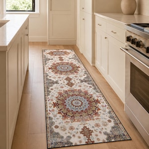 Peut inclure: Un long tapis de couloir rectangulaire au fond crème, orné de motifs circulaires répétitifs dans des tons de rouge rouille, bleu sourd et gris anthracite. Le tapis présente une bordure sombre et une finition vieillie sur tout le motif.