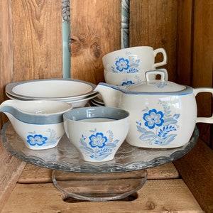 Könnte beinhalten: Ein Vintage-Tee-Set mit einem blauen und weißen Blumenmuster. Das Set enthält eine Teekanne, eine Milchkännchen, eine Zuckerdose und zwei Teetassen. Die Teetassen und die Teekanne haben einen grauen Rand.