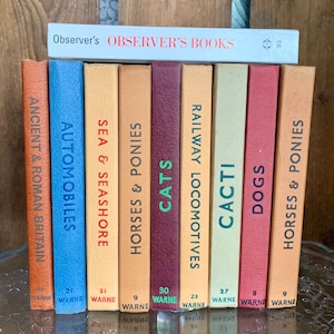 May include: A set of nine vintage hardcover books with colorful spines. The books are part of the "Observer's Books" series and feature titles like "Ancient & Roman Britain", "Automobiles", "Sea & Seashore", "Horses & Ponies", "Cats", "Railway Locomotives", "Cacti", "Dogs", and "Horses & Ponies".