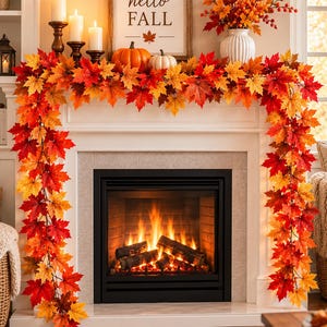 May include: A fireplace mantel decorated with an artificial maple leaf garland in shades of red, orange, and yellow. The display includes three white pillar candles, two pumpkins, a sign reading hello FALL, and a vase of autumn foliage.