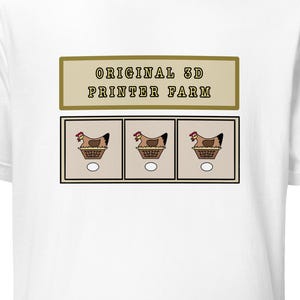 May include: A white short-sleeve t-shirt featuring a graphic print with the text "ORIGINAL 3D PRINTER FARM" above three square panels, each containing an illustration of a brown chicken sitting in a basket with a single white egg below it.