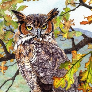 May include: A brown and gray great horned owl with yellow eyes perched on a branch of a tree with yellow and green leaves. The owl is looking directly at the viewer.