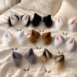 May include: A collection of nine animal ear headbands featuring faux fur in various colours including black, white, brown, grey, and tan. Each headband has two pointed ears with soft, plush textures and thin metal bands for secure placement.