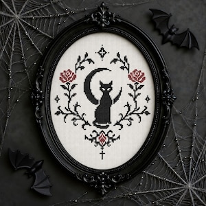 May include: An oval black frame containing a cross-stitch embroidery on white fabric. The design features a black cat silhouette in front of a crescent moon, flanked by two red roses with black stems, and a small cross symbol at the bottom center.