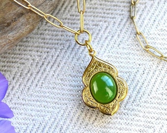 May include: A gold chain necklace with a green gemstone pendant. The pendant is in a detailed, ornate design.