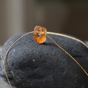 May include: A delicate gold chain necklace with a single, raw, orange-brown gemstone pendant.
