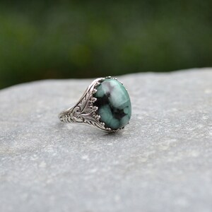May include: A silver ring with an oval-shaped green gemstone set in a detailed filigree design.