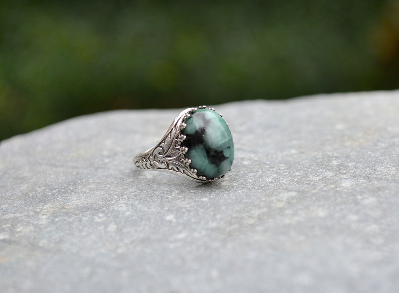 May include: A silver ring with an oval-shaped green gemstone set in a detailed filigree design.