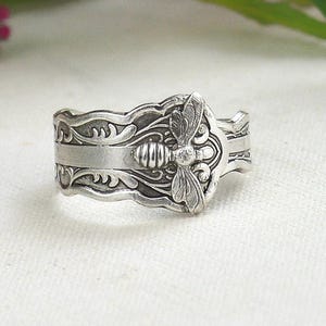 May include: Silver ring with a detailed bee design. The ring is made from a repurposed vintage spoon.