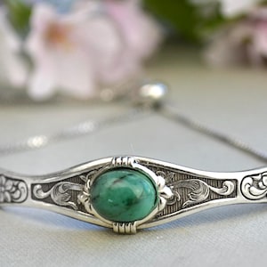May include: A silver bracelet with an ornate design and a green gemstone. The bracelet has a sliding clasp.