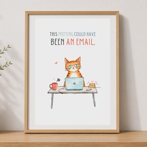 May include: A framed wall art print featuring an illustration of an orange tabby cat sitting at a desk with a laptop, a red mug, and an envelope. The text reads, THIS MEETING COULD HAVE BEEN AN EMAIL. The frame is light wood with a white mat border.