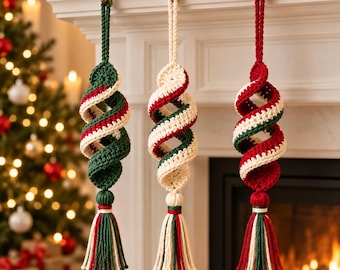 Op de afbeelding: Drie hangende spiraalvormige ornamenten gemaakt van gehaakt garen in rood, groen en crème. Elk ornament heeft een gedraaid, kurkentrekkerachtig lichaam dat aan een bijpassende lus hangt en is afgewerkt met een decoratieve, meerkleurige kwast.