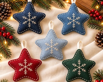 Op de afbeelding: Vijf stervormige stoffen ornamenten met geborduurde witte sneeuwvlokken en wit gestikte randen. De set bevat een donkerblauw, medium blauw, lichtblauw, rood en donkergroen ornament, elk voorzien van een klein wit lusje om op te hangen.
