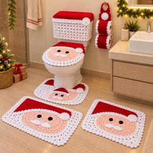 May include: A crochet bathroom set featuring a Santa Claus theme with red, white, and peach yarn. The set includes a toilet tank cover, a toilet seat cover, a toilet rug, a floor mat, and a hanging toilet paper holder, all with Santa face designs.
