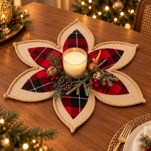 May include: A flower-shaped table centerpiece featuring a red and black plaid fabric inlay surrounded by a tan burlap border with rope trim. A glass candle holder with a white wax candle sits in the center, accented by pine needles, pinecones, and small metal bells.