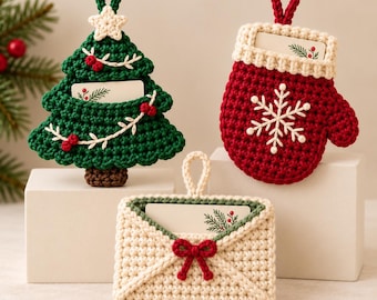 Op de afbeelding: Drie gehaakte ornamenten bestaande uit een donkergroene kerstboom met een witte ster, een rode want met een witte sneeuwvlok en een crèmekleurige envelop met een rode strik. Elk item heeft een ophanglus en een kleine kaart.