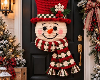 May include: A crocheted snowman door hanging featuring a red top hat with a green and white checkered band, a white face with black eyes, a carrot-colored nose, and pink cheeks, wearing a long red, green, and white checkered scarf with tassels.